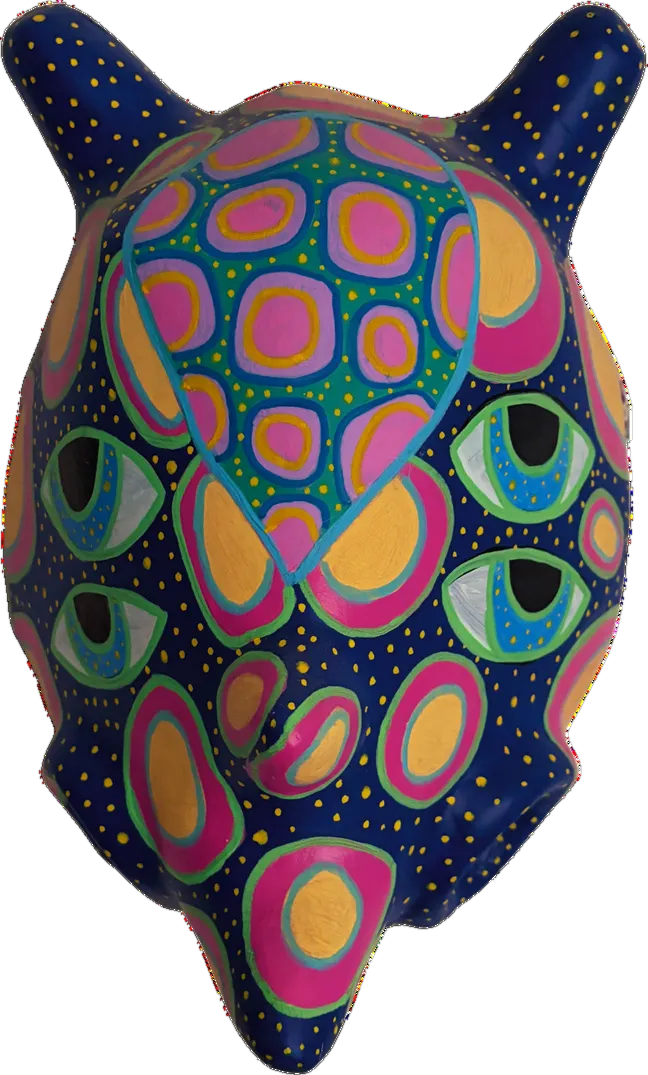 Máscara con orejas puntiagudas pintada en azul profundo con óvalos concéntricos en rosa, amarillo y turquesa.